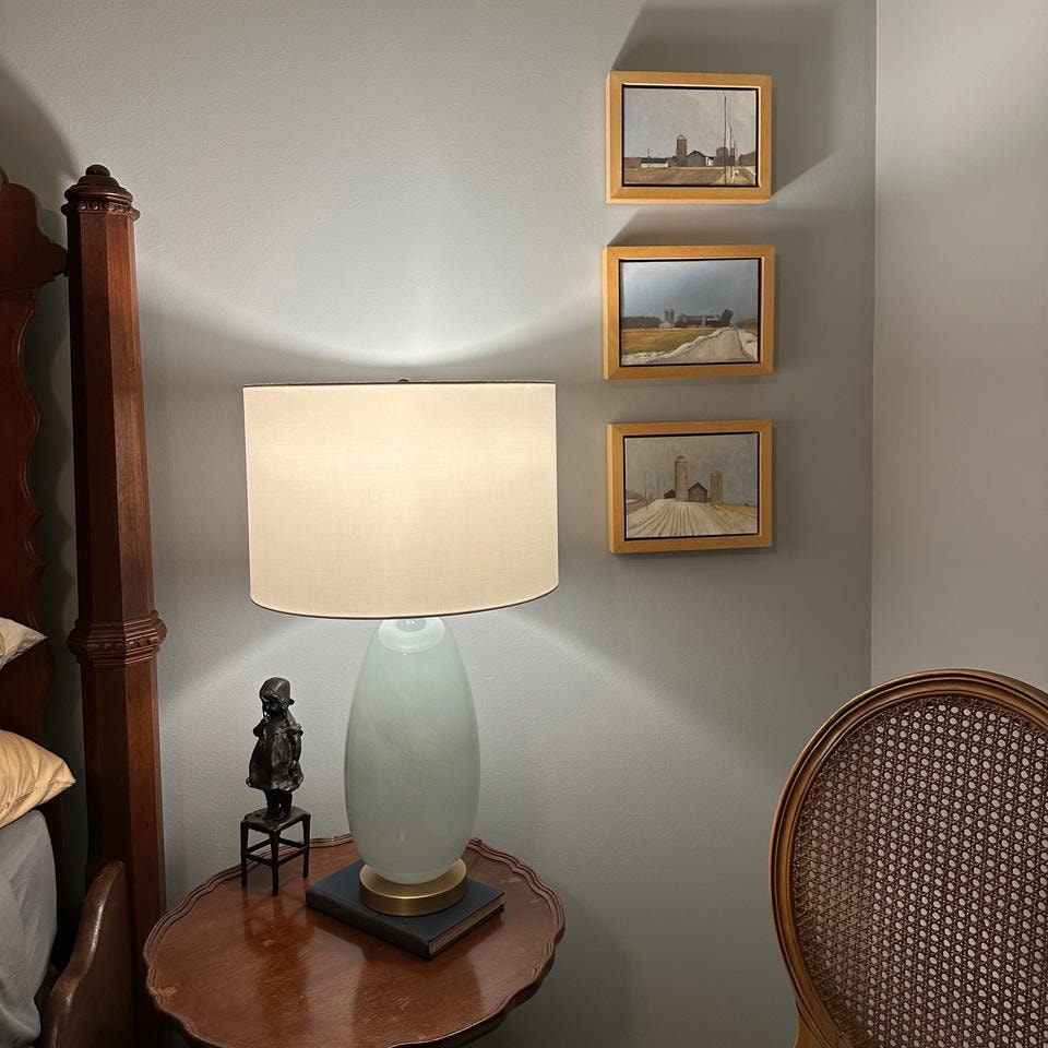 Brentwood Cove — After, nightstand with celadon lamp, bronze figurine and three framed landscape paintings