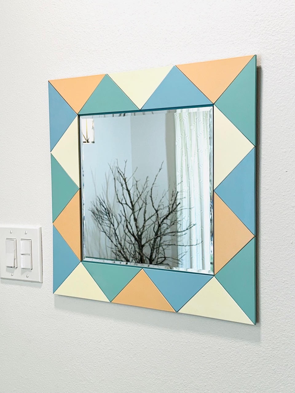 Square mirror with geometric triangular frame in teal, cream and peach tones