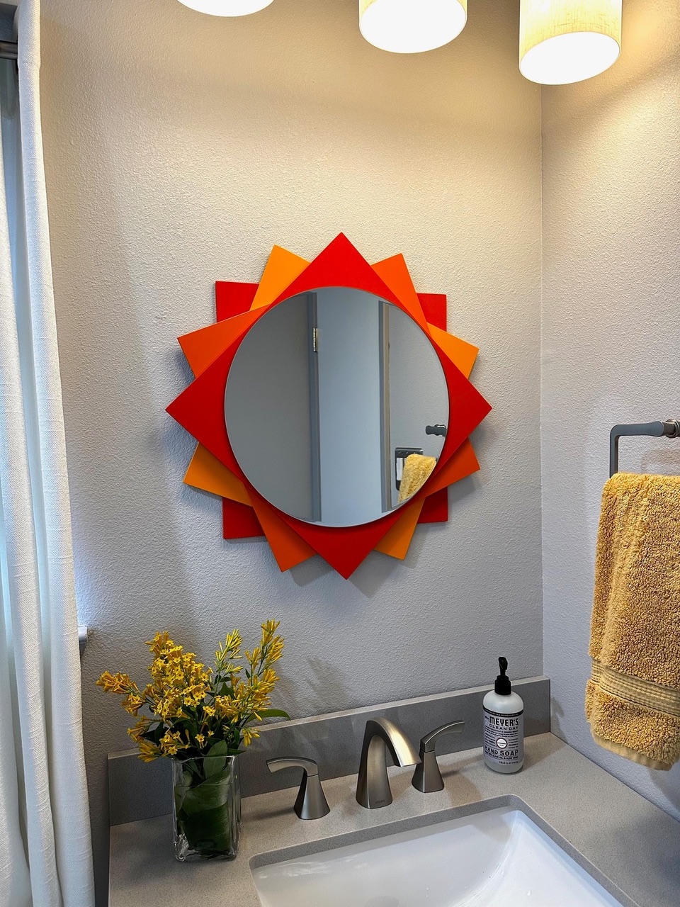 Round starburst mirror with red and orange layered points in bathroom setting
