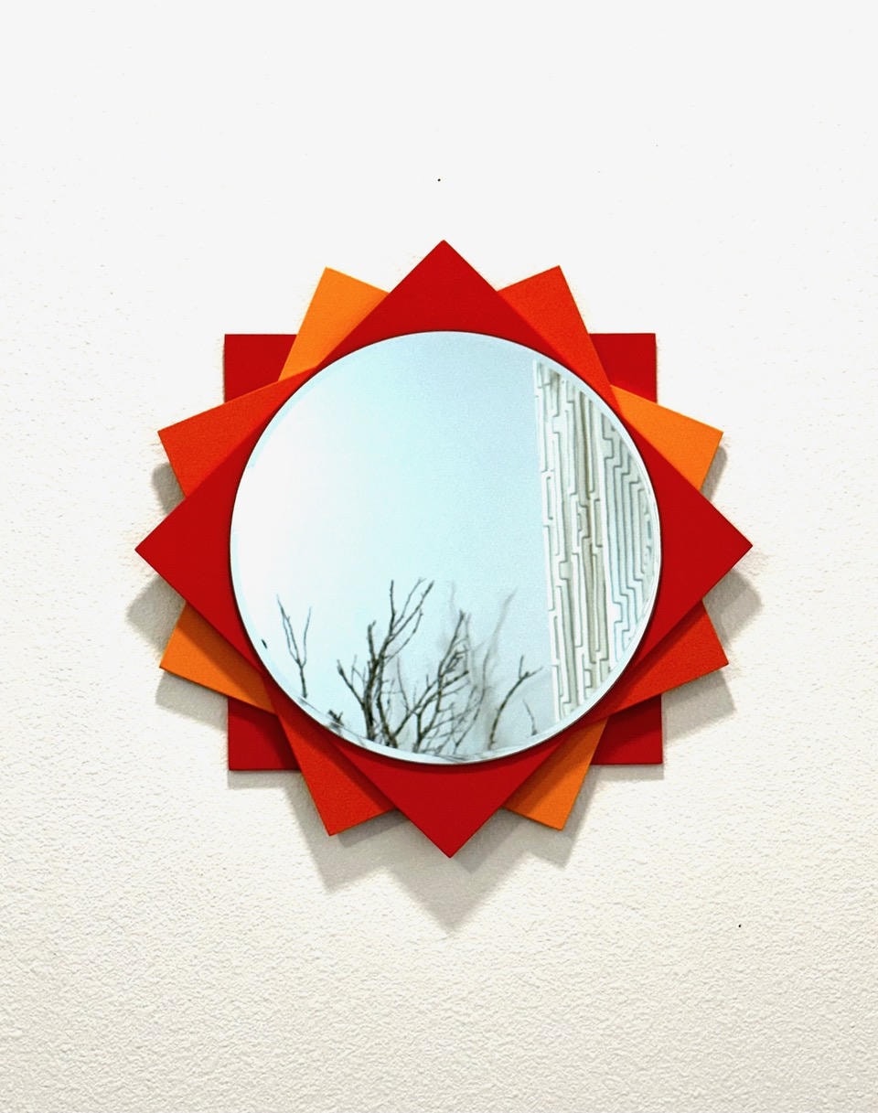 Round starburst mirror with red and orange layered points on white wall