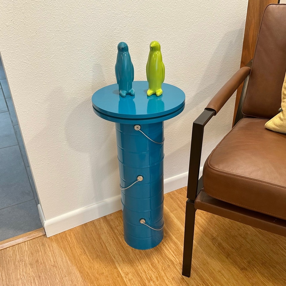 Blue paint can pedestal table with teal and lime ceramic penguin figurines on top