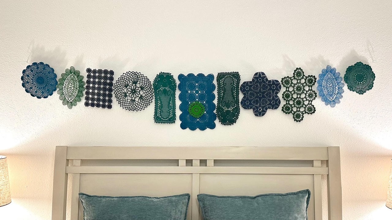 Decorative lace doilies in teal, green, navy and blue tones displayed above a bed