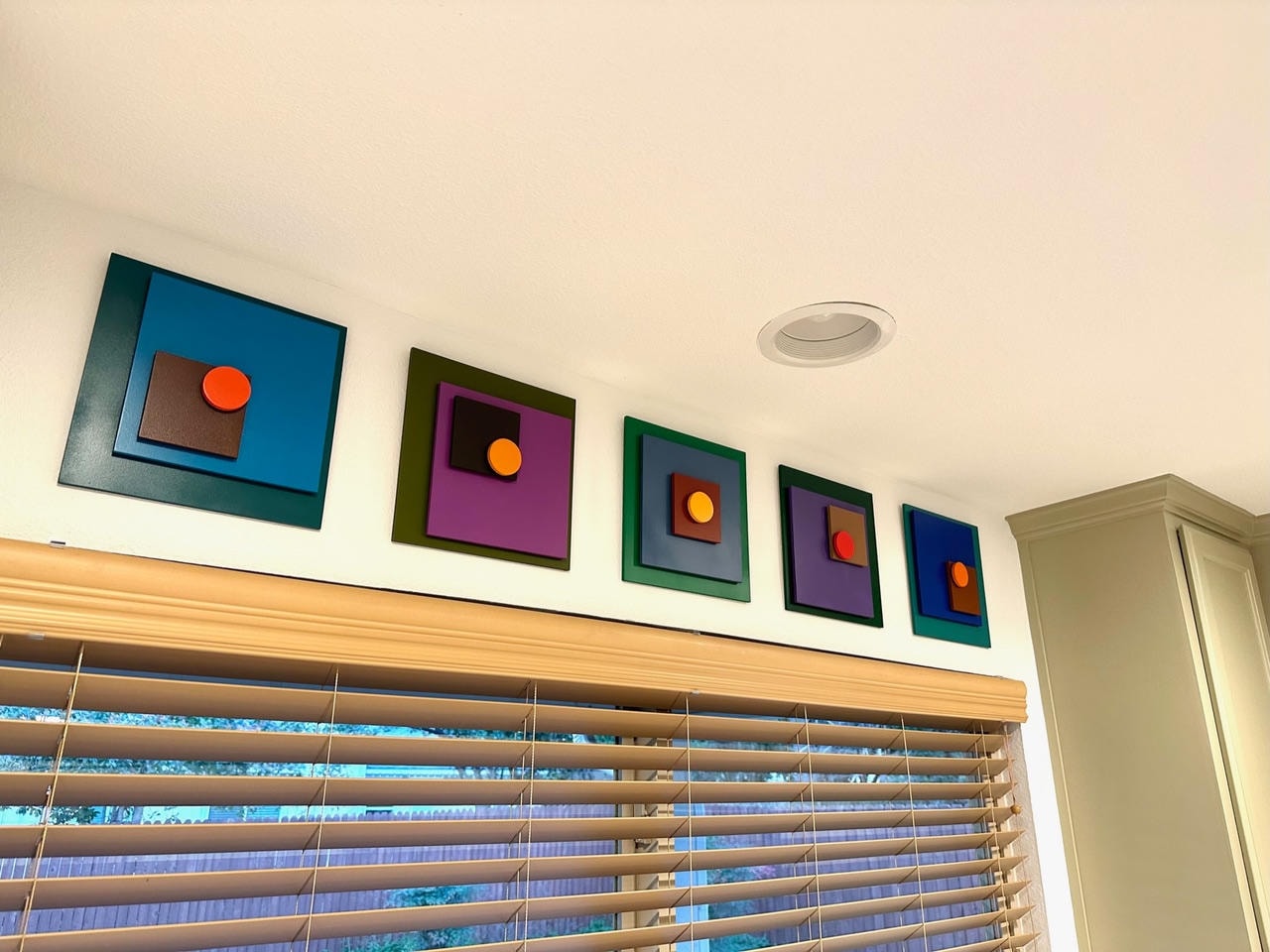 Five colorful nested geometric frame wall art pieces with illuminated spheres above a window