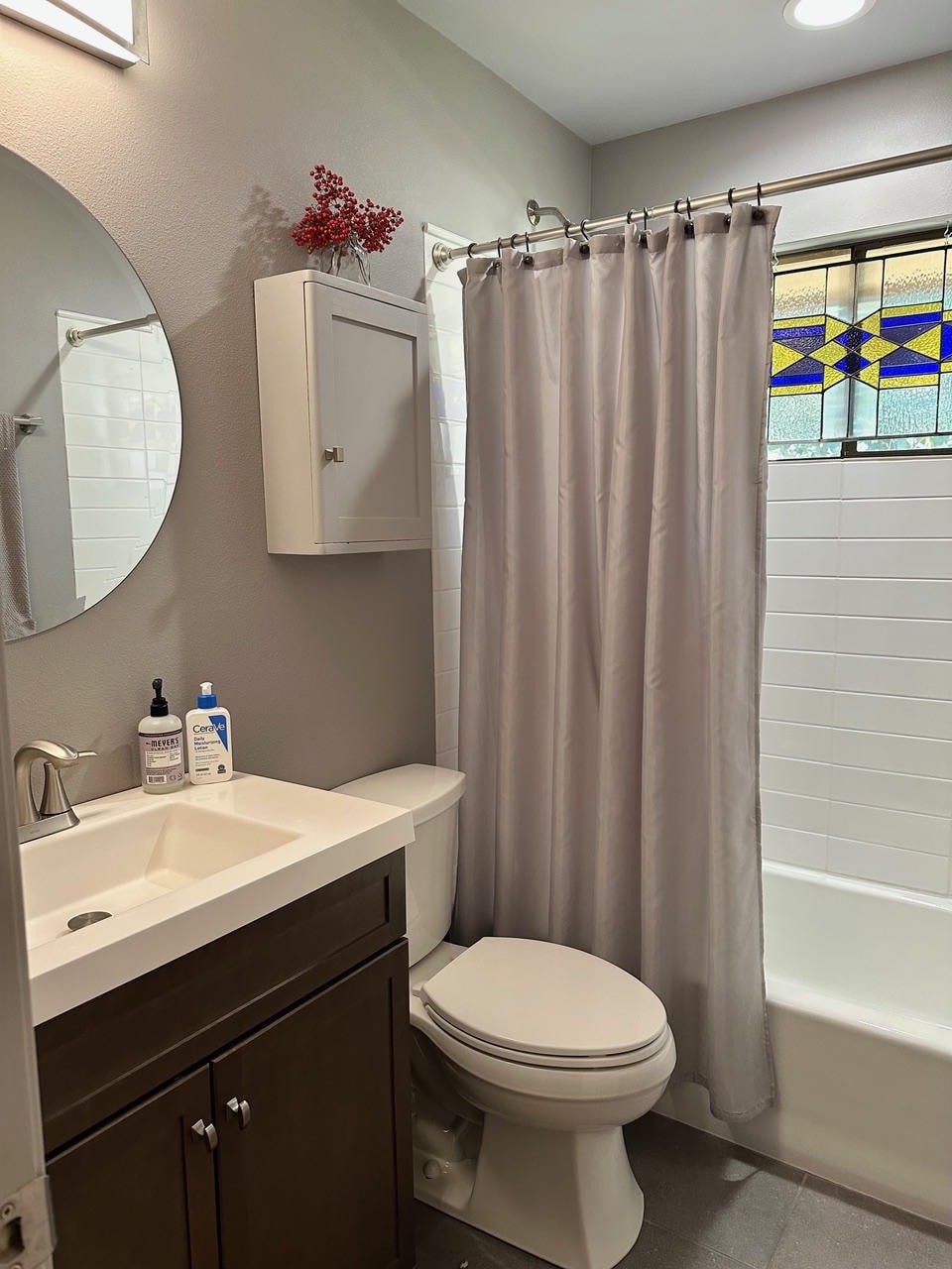 Austin Rock — After, bathroom with dark vanity, round mirror and stained glass window