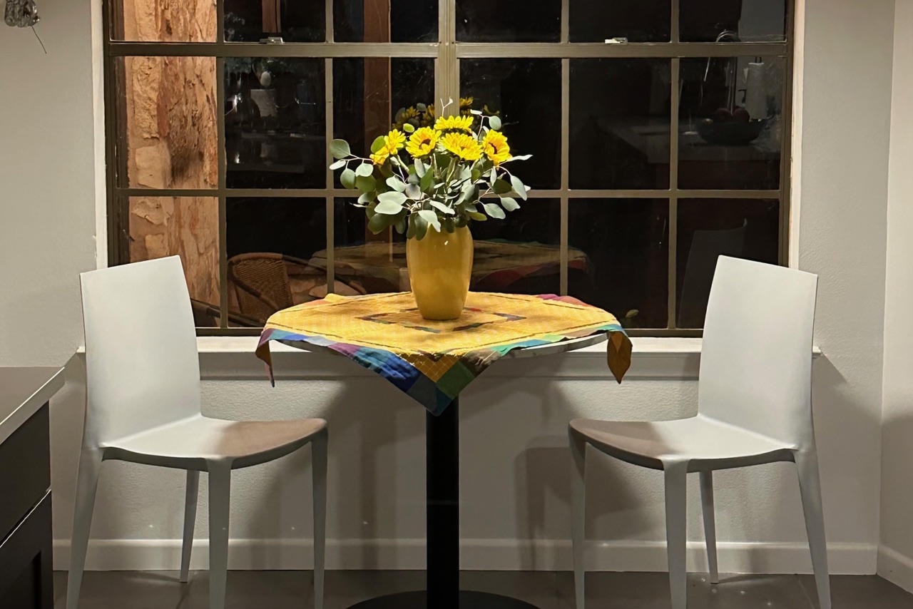 Austin Rock — After, dining nook with white chairs, yellow flowers and colorful tablecloth