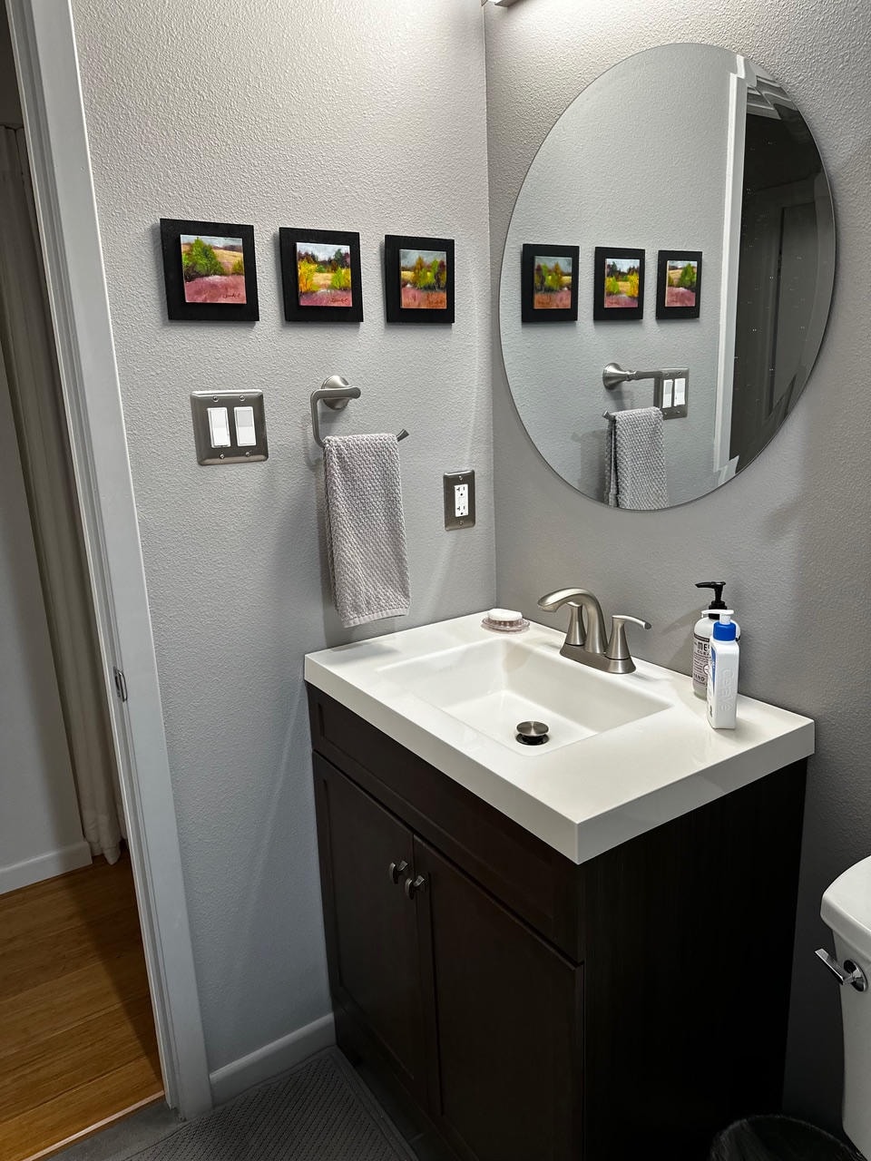Austin Rock — After, bathroom with dark vanity, round mirror and landscape art panels